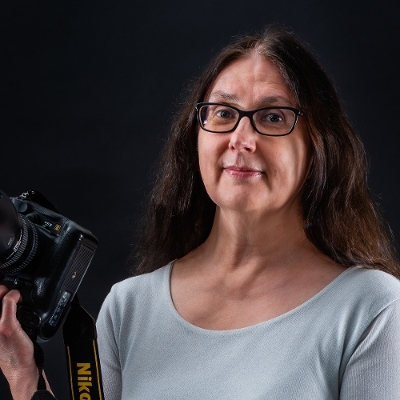 Head shot of Sue holding a black camera